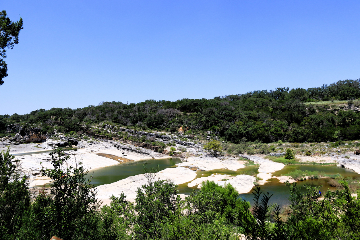 Scenic view of a rocky riverbed with lush greenery and a clear blue sky at Pedernales Falls State Park, Texas