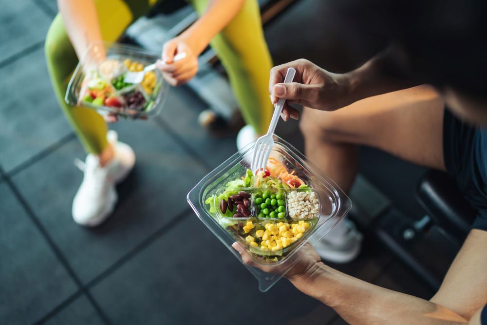 Top view Asian man and woman healthy eating salad after exercise at fitness gym. Two athlete eating salad for health together. Selective focus on salad bowl on hand